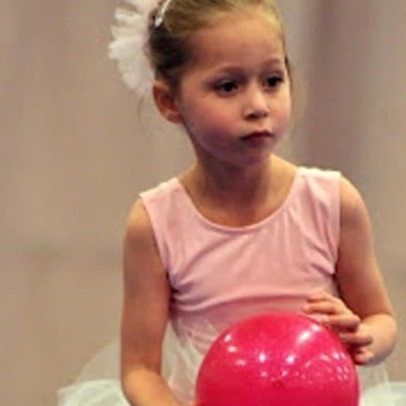 Young preschool student in pink leotard holding pink ball