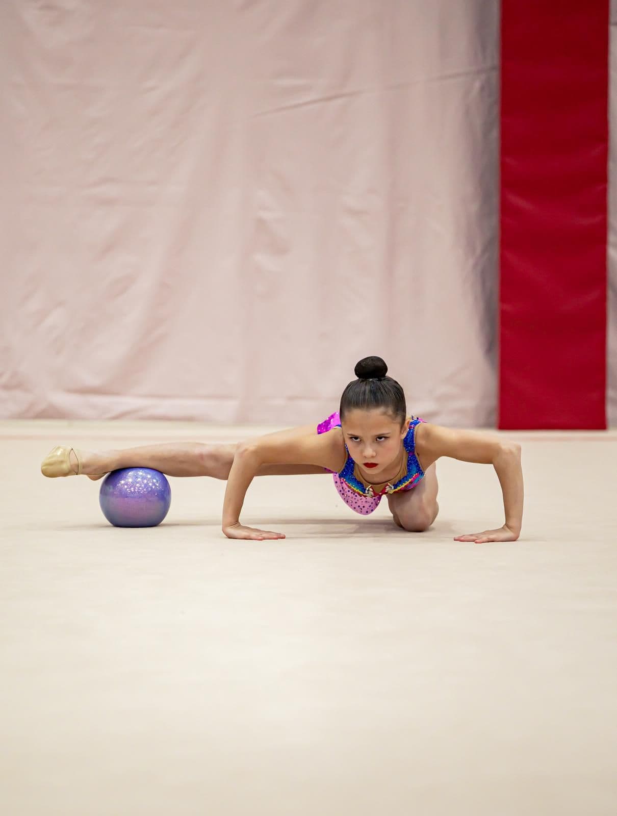 Young gymnast performing floor pose with ball at competition