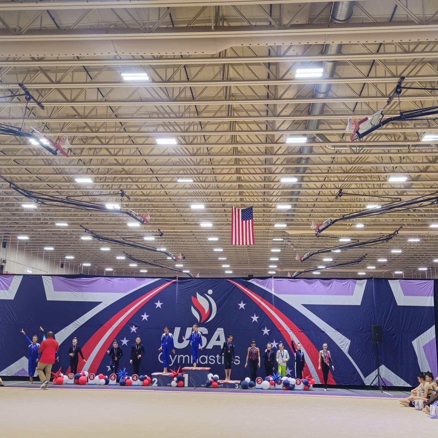 Wide view of the awards podium under the USA Gymnastics banner at the 2026 USAG Rhythmic Elite Qualifier