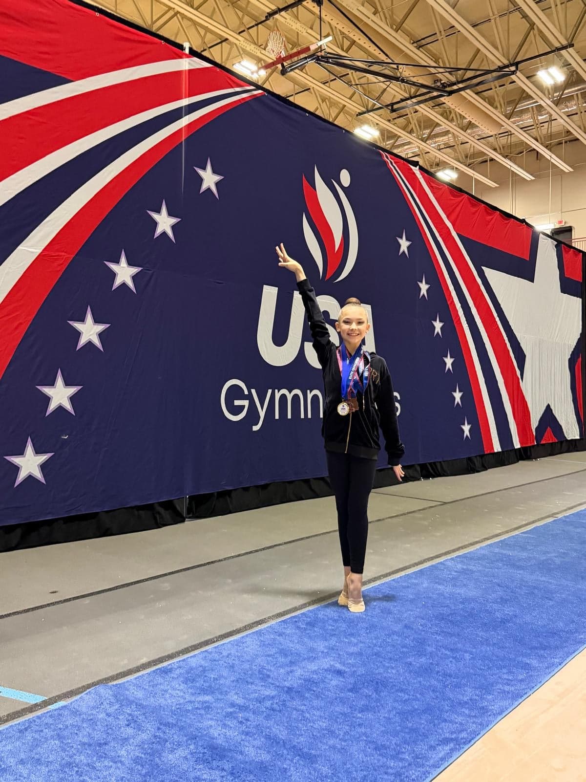 RRT athlete posing with two medals at the USA Gymnastics backdrop during the 2026 Rhythmic Elite Qualifier