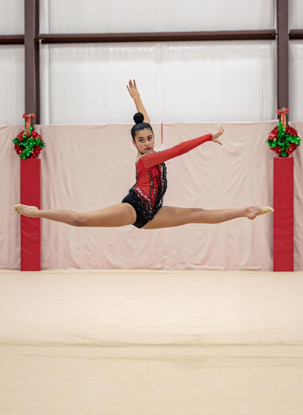 Gymnast performing split leap in red leotard at holiday competition