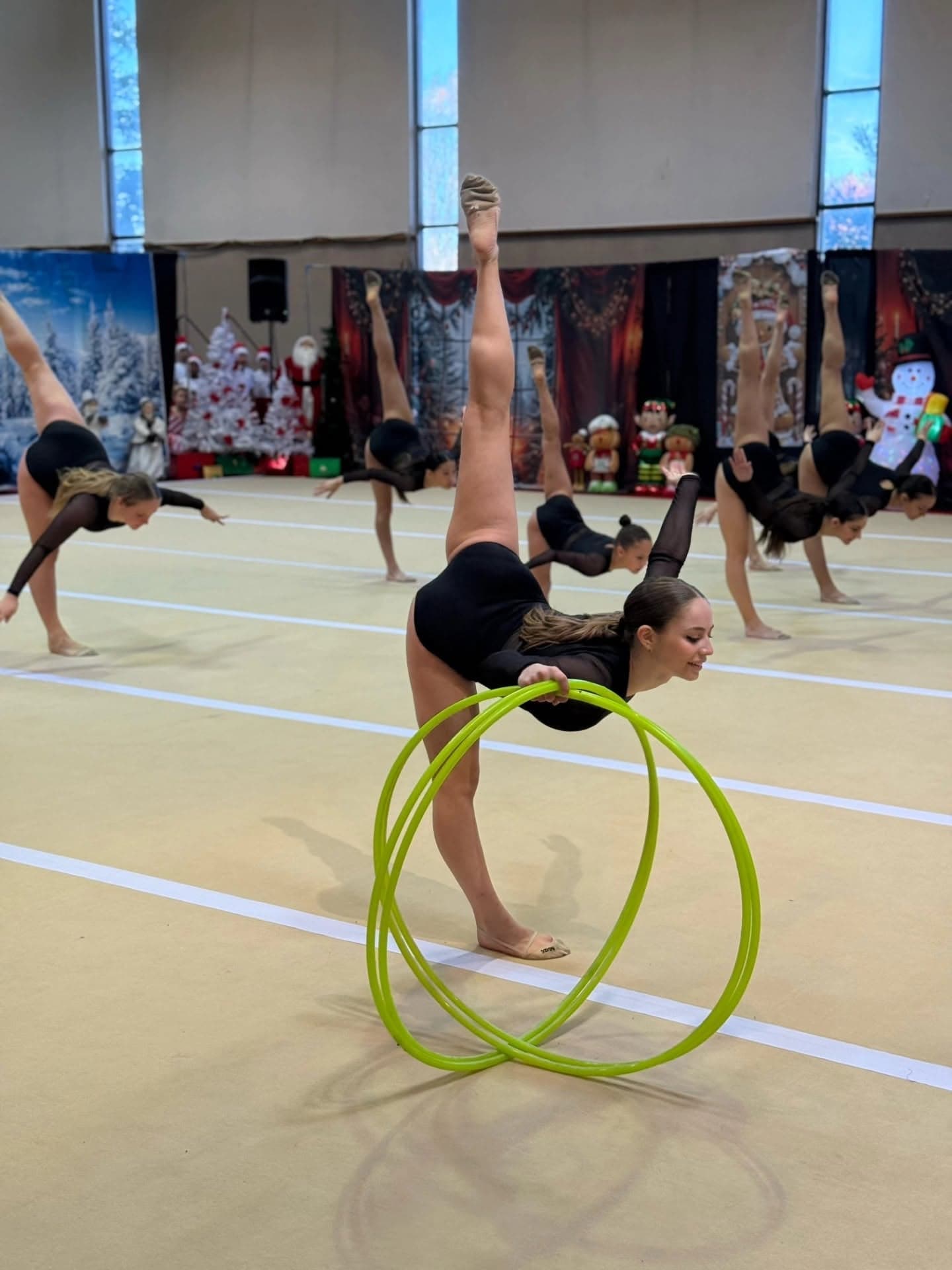 Gymnasts hold arabesques around a stack of hoops during a holiday showcase routine