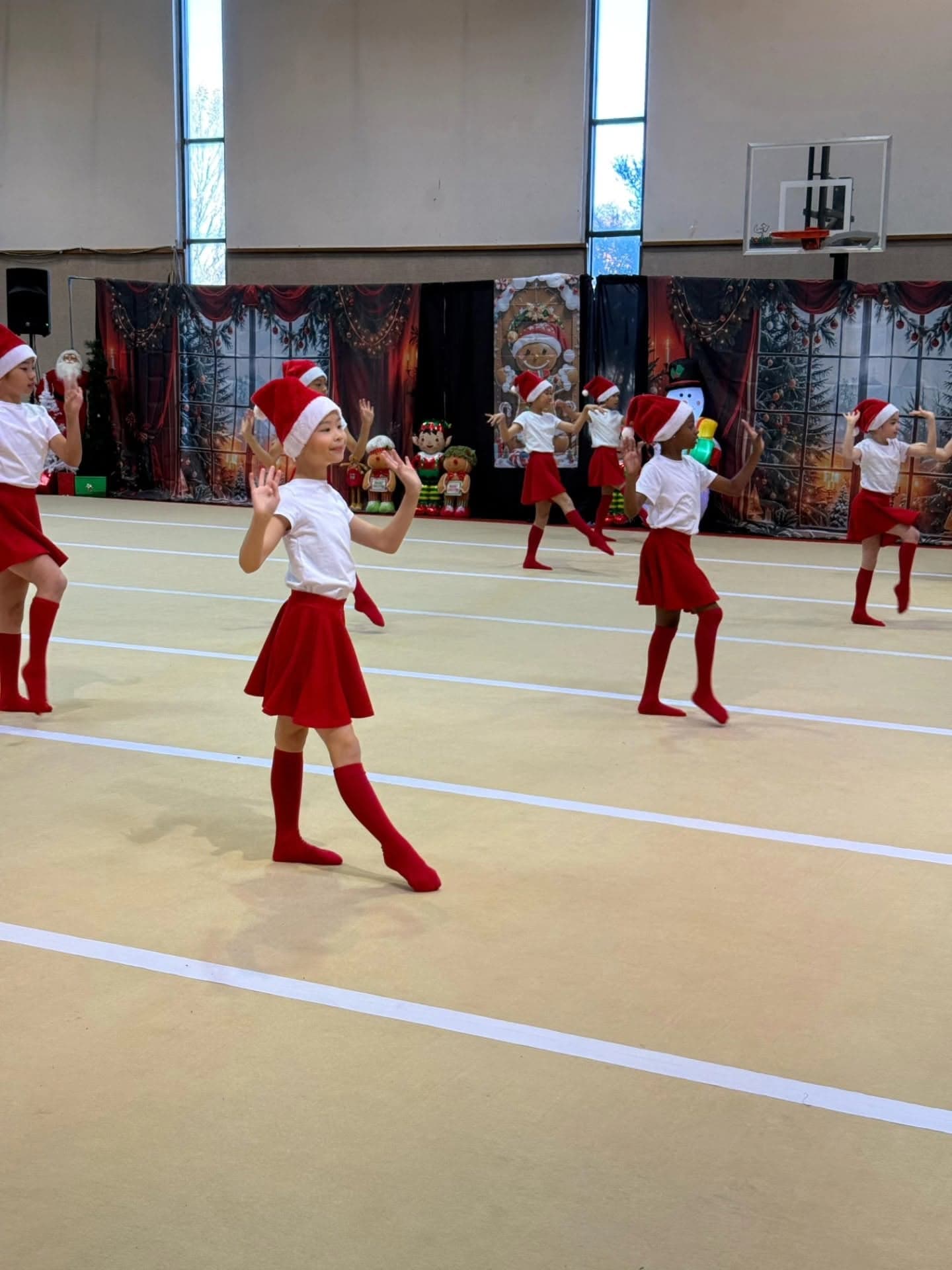 Young gymnasts in Santa hats and red skirts perform at a holiday showcase