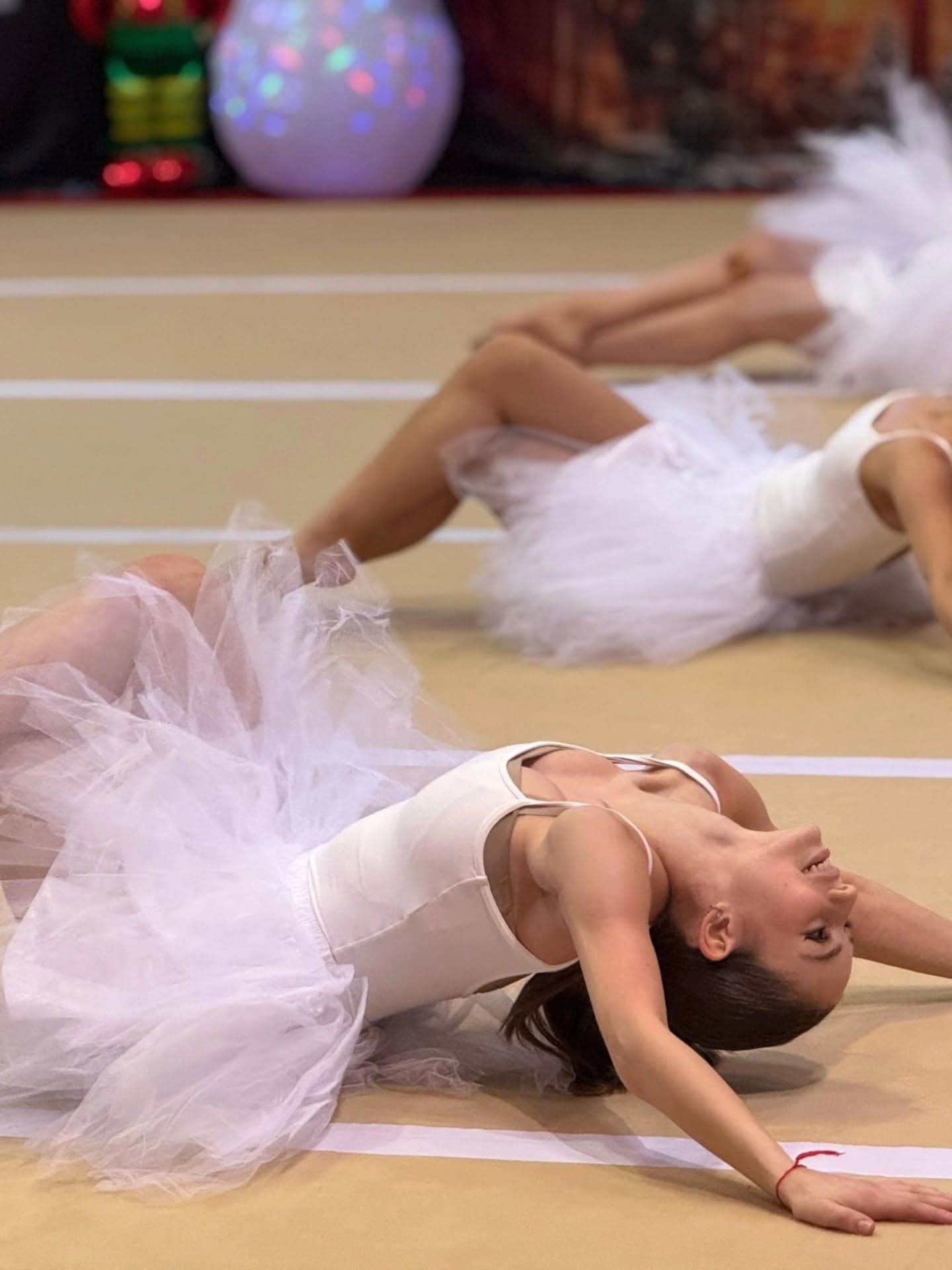 Gymnasts in white tutus arch into backbends during a holiday showcase ballet number