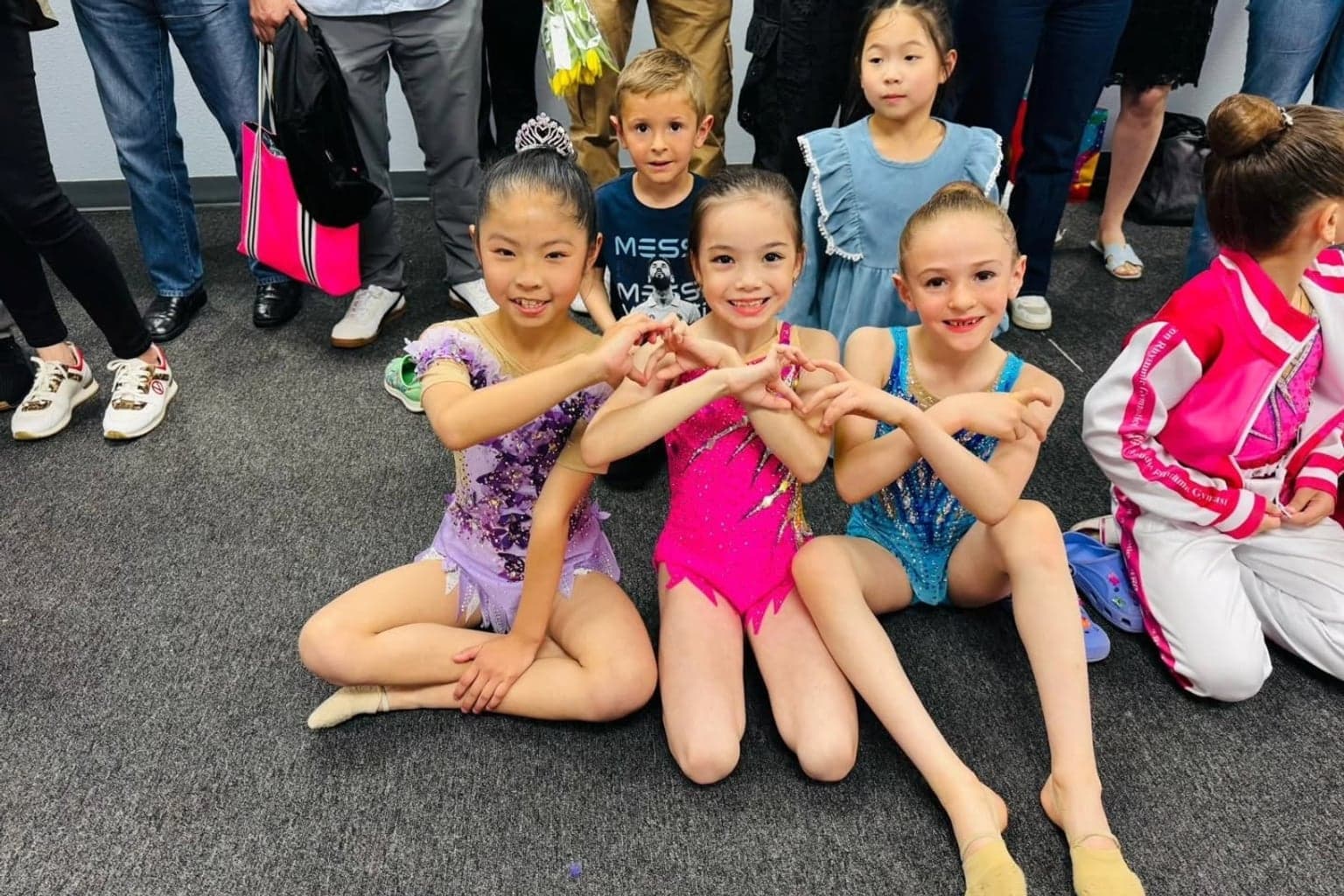 Three young gymnasts in competition leotards making heart hands together at a meet