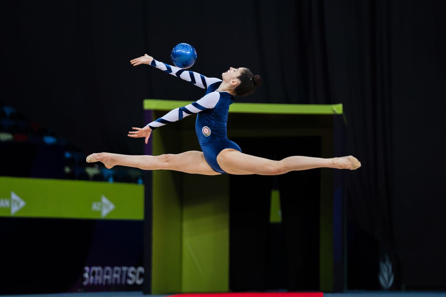 Rhythmic gymnast performing a split leap with a ball during an arena competition