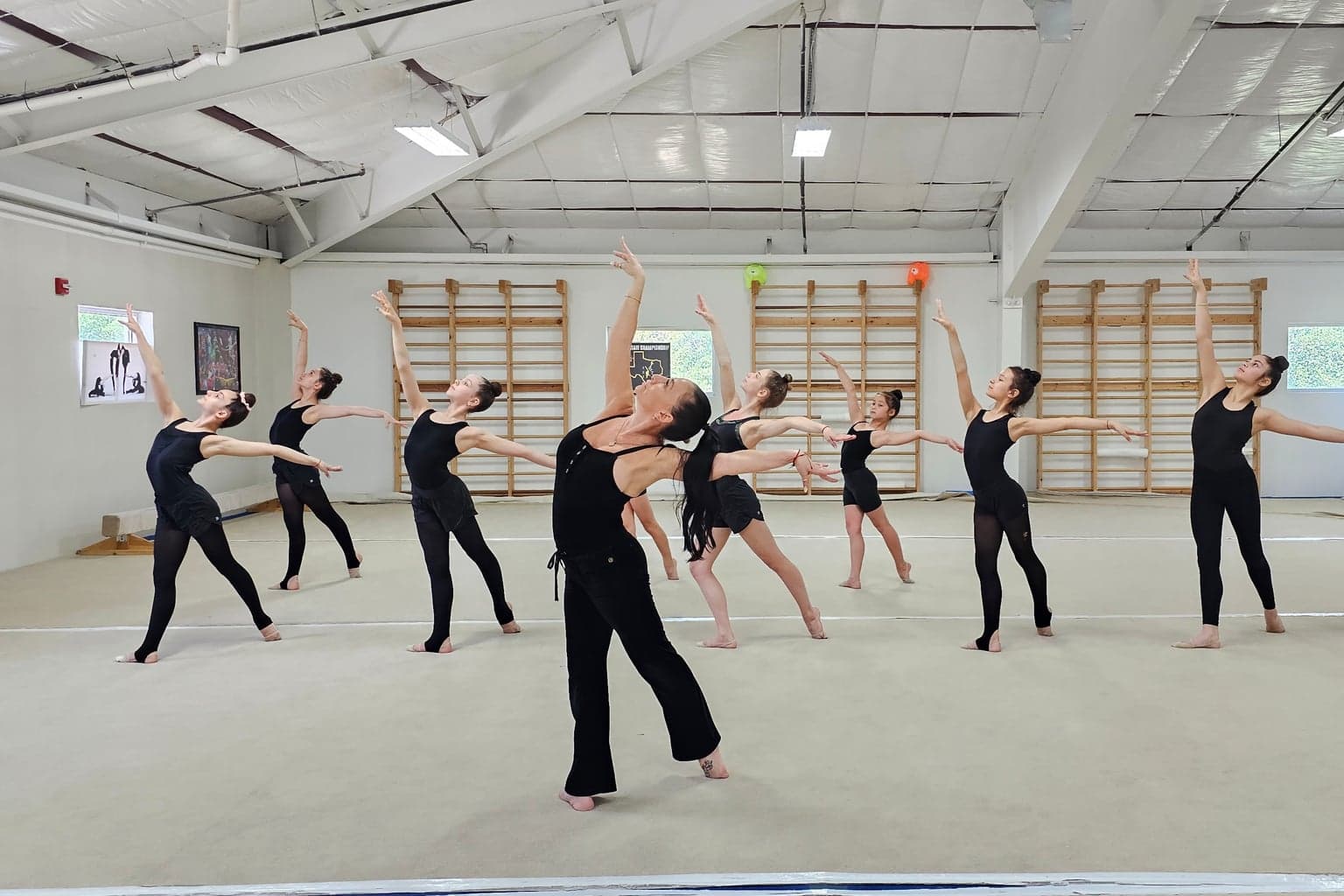 Coach Ella leading students in black practice wear through a dance pose in the studio