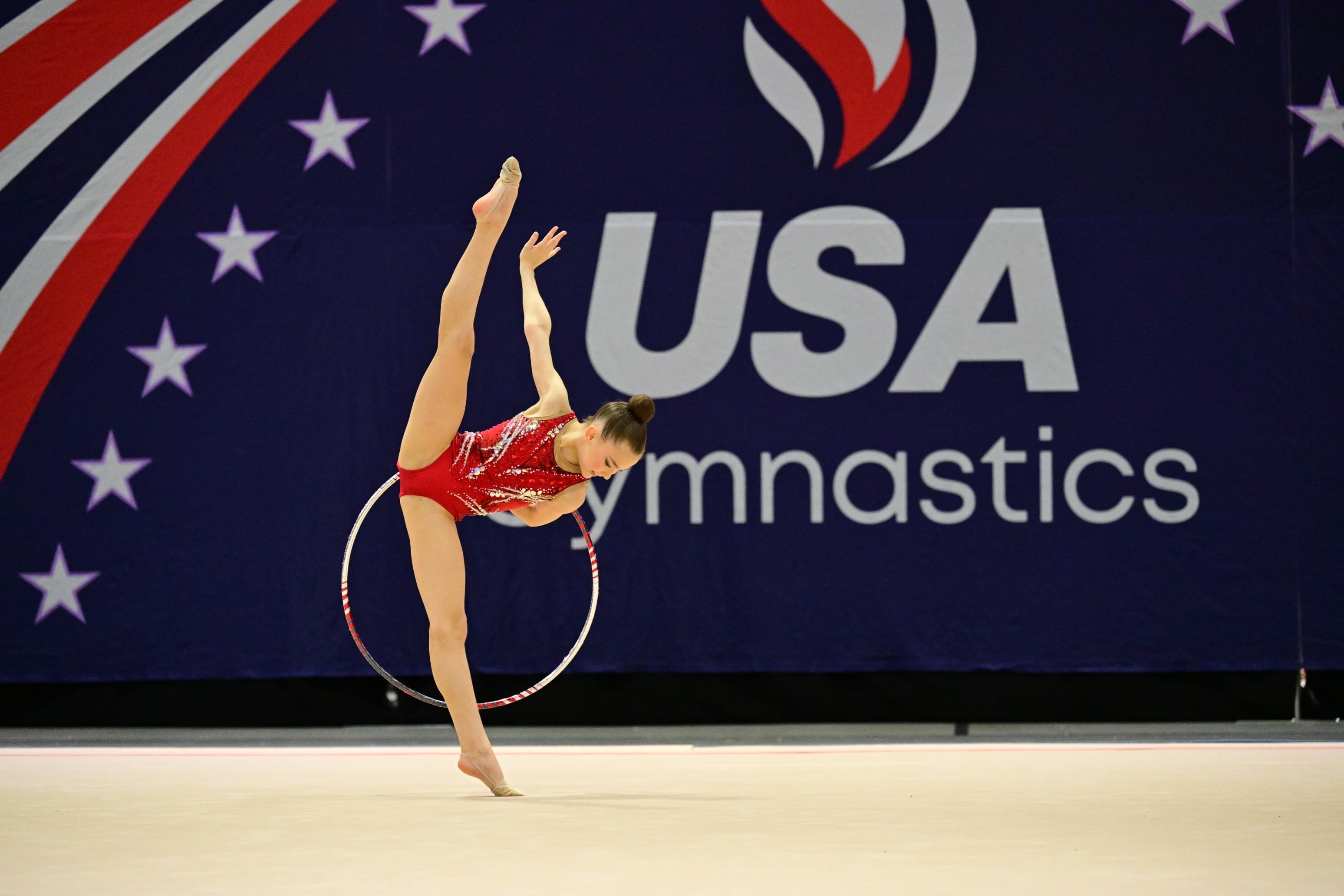 Rhythmic gymnast performing a balance skill with a hoop during competition.